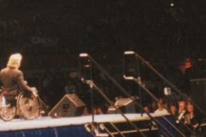 Man in a wheelchair standing on a stage speaking to a crowd.