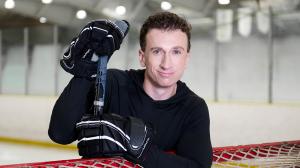 Portrait of Brock McGillis standing at a hockey net in an arena, holding his stick while promoting the Shiftmakers Tour.