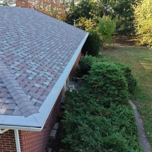 Angled aerial photo showing multi-tone asphalt shingles and white seamless gutters with guards on a brick home beside trees in Toledo, installed by All Exterior Solutions.