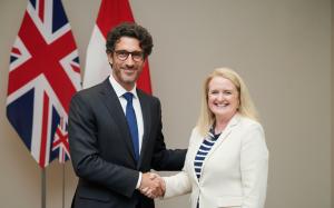 Official handshake between Darren Brown, Executive Director of The Schools Trust (UK), and Eileen Fisher, Head of School at The Independent School of Jakarta (ISJ). They are standing at a press conference podium in suits with the British Union Jack and In