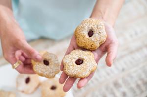 Two hands holding flower-shaped Cooee Cookies dusted with icing sugar and filled with native fruit jam.