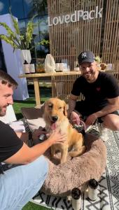 LovedPack founders Elbano and James with a golden retriever at PetCon LA, deomonstrating the brand's Whole Care ritual shampoo and conditioner, a gentle skin-loving wash that gives back to resuce dogs through its Wash-for-a-Wash mission.