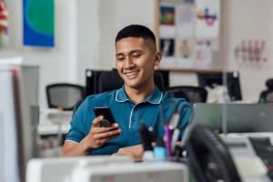 Men sitting in office looking at phone, wearing a polo shirt
