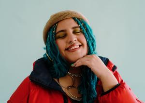 Woman with teal hair and beanie smiling confidently, representing neurodivergent celebration and authentic self-expression in mental healthcare