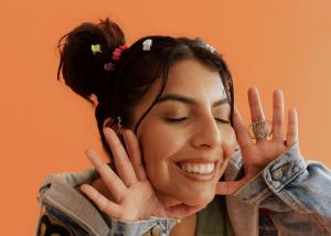 Joyful woman with colorful hair accessories smiling broadly against orange background, expressing hope and positive mental health outcomes