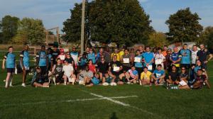 A large group of Rainbow Griffins Rugby Club players and supporters posing together on a sunny field, holding certificates and rugby balls, with trees and playground equipment in the background.