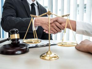 Professional handshake between attorney and client across desk with gavel and scales of justice, symbolizing Clark Meyers PC's partnership approach to legal services and commitment to direct partner access, personalized attention, and strategic business c