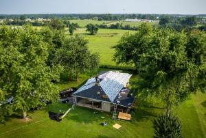 Aerial view of a roofing crew installing new shingles and underlayment on a single-story home surrounded by trees and farmland in Missouri.