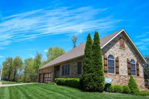 Front view of a brick home with a newly installed shingle roof, surrounded by trees and a well-kept lawn under a bright blue sky.