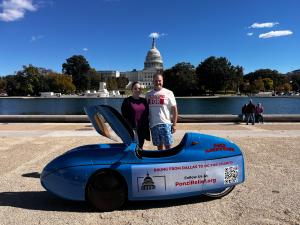 The Novinger's standing in front of the U.S. Capital Building in Washington DC, next to the bright blue velomobile during their 2,000-mile charity ride, “Pedaling Against Ponzi’s,” to support victims of financial fraud.