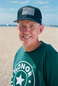 Sam Evans is wearing an Honor US Vets t-shirt and hat and smiling at the camera