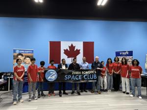A group of students and mentors from Zebra Robotics stand proudly holding a “Zebra Robotics Space Club” banner in front of a large Canadian flag, celebrating the launch of the new Space Club initiative.