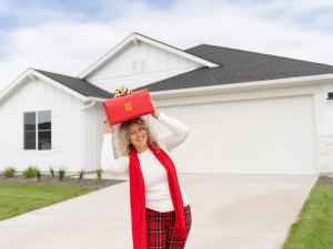 Woman stands in front of a new home for sale with a present for the CBH Festival of Homes launch.