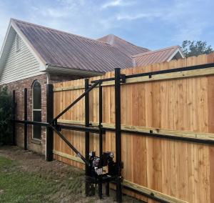 Automatic driveway gate attached to a wood privacy fence at a Louisiana home.