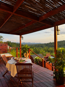 Scenic outdoor dining setup on a wooden deck with a table set for two, overlooking forested hills and a sunset sky in the North Georgia mountains.