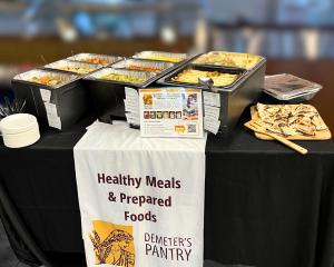 Demeter’s Pantry foodservice display featuring ready-to-serve trays of clean-label meals and a branded banner reading “Healthy Meals & Prepared Foods.”
