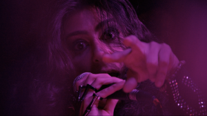 Close-up of Farrah Mechael singing into a microphone under magenta stage lighting during her Halloween Eve show.