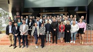 A group of 45 men and women stand on a five-step red staircase in three rows, posing for a photo in front of a black and grey building at the University of Łódź.