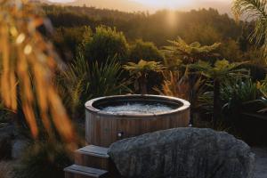 An outdoor hot tub nestled in lush native bush at Domu Retreat, steam rising through the trees in soft morning light, evoking calm and seclusion.