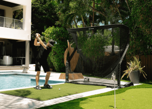 An adult male at the top of his swing, about to hit a golf ball into a golf net outdoors.