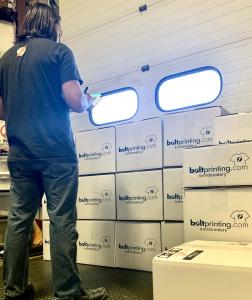 Bolt Printing employee organizing boxes for UPS Ground shipments inside company warehouse during 50% off shipping promotion.