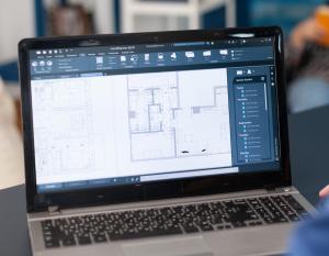 Blueprint on a laptop with a woman in the background.