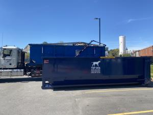 Top Dog roll-off dumpsters are ready for delivery, with one loaded on a truck and another positioned on the ground.