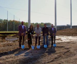 Three men and one woman stand with shovels to symbolize a groundbreaking for a convenience store.