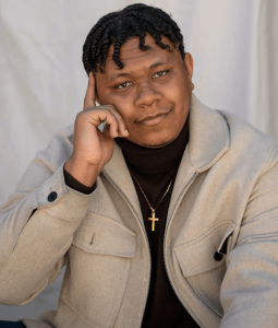 Portrait of composer Jonathan Corbie wearing a beige jacket and black turtleneck, smiling thoughtfully at the camera.
