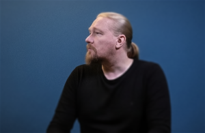 A long-haired and bearded man's (Esa Linna) profile photo against blue background