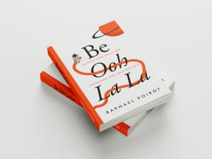 Two stacked copies of the book Be Ooh La La by Raphael Poirot, featuring an orange-and-white cover with an astronaut riding a rocket and the subtitle “Achieve Your Goals and Transform Into Your Best Self.”