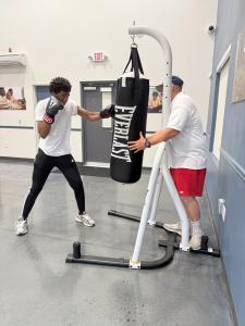 A boxing coach teaches a student bag-work