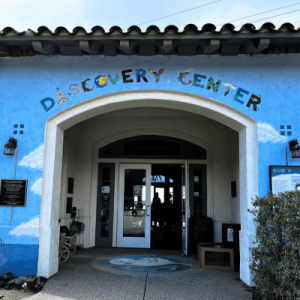 Entrance of the Discovery Center, featuring a blue wall with clouds and colorful letters above the door, inviting exploration.