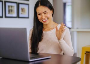 Woman smiling and waving during a video call on laptop at home, representing accessible telehealth mental health counseling services for families seeking professional support.