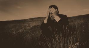 Younger man, sitting alone in a grass field, black and white photo, holding his head sad and in grief