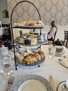 A three-tier stand filled with scones, tea sandwiches, and preserves sits on a table set for afternoon tea inside The London Tea Room, with patterned wallpaper and guests in the background.