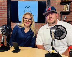 Photo of a woman and a man sitting at a podcast studio desk