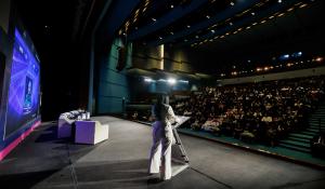 A woman stands speaking to an audience during the Creative Women Forum Saudi Arabia 2025 in Riyadh, inspiring attendees on leadership and innovation.