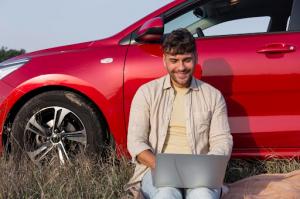 Student sitting beside a red car using a laptop to complete Get Drivers Ed’s online driving course, representing convenient and flexible driver education.