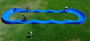 Aerial view of several people riding bikes on a blue modular pump track, showing how the track accommodates multiple ages and riders at once.