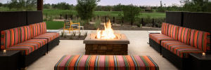 Cozy outdoor seating area with colorful striped cushions surrounding a stone fire pit, set against a lush green landscape.