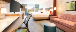 Modern hotel room featuring two beds, a cozy sofa, desk area, and large windows revealing a scenic outdoor view.