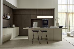 Modern European kitchen with tall dark wood cabinets, greige island with two black stools and a large window with sheer curtains.