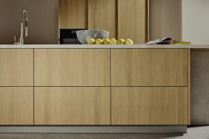 Close view of flat oak cabinet fronts on a kitchen island with light countertop, modern faucet, stone bowl and green apples.