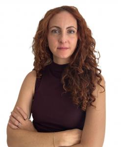 Portrait of Jessica Abouzeid, senior executive at EssilorLuxottica, standing with arms crossed against a white background.