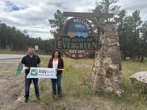 TidyTask Founder Carl Dupper and Cassandra Loman, franchise owner of TidyTask Evergreen, pose in with a TidyTask sign in front of the Evergreen community's sign.