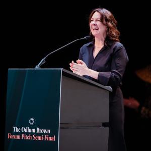 Kirsten Koppang Telford, CEO of The Forum stands behind a podium, speaking into a microphone. The podium has text that reads: Odlum Brown Forum Pitch Semi Final