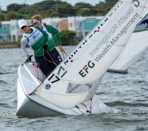 Two sailors, Drew Lamm and Lillie Kniskern, hiking out on a small sailboat (FJ or 420 dinghy) during a regatta.