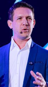 Rony Jabour, a Brazilian USA-based safety professional, speaking on stage with a headset microphone, wearing a blue blazer and white shirt during a keynote presentation.