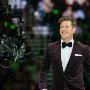 Wellness expert, Gordon Fraser, smiles broadly into the lens a video camera as he walks across the stage of MGM Arena at a celebratory event